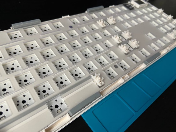 Разобранная база клавиатуры: видны серые демпферы по краям, обеспечивающие подвижное крепление gasket mount.