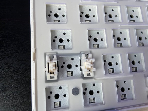 Белые пластиковые стабилизаторы для длинных клавиш, установленные на металлическую пластину клавиатуры.