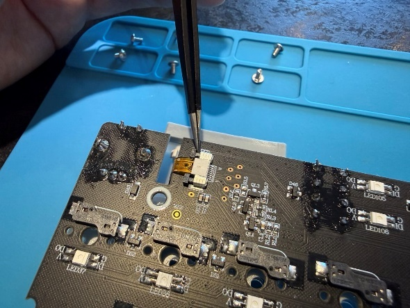 Отключение желтого шлейфа экрана клавиатуры на печатной плате с помощью пинцета.