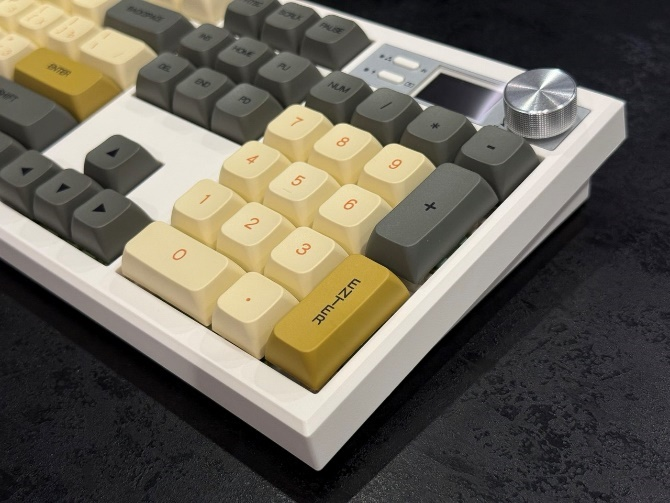 Левый нижний угол собранной кастомной клавиатуры крупным планом: установлены серо-бежевые колпачки с золотистыми акцентами.