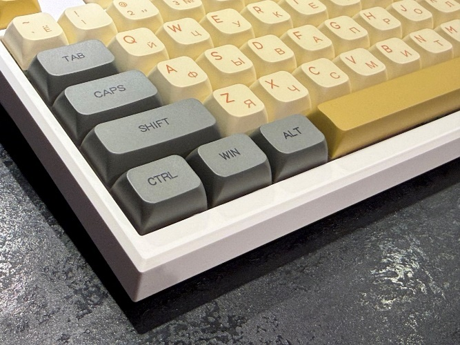 Левый нижний угол собранной кастомной клавиатуры крупным планом: установлены серо-бежевые колпачки с золотистыми акцентами.