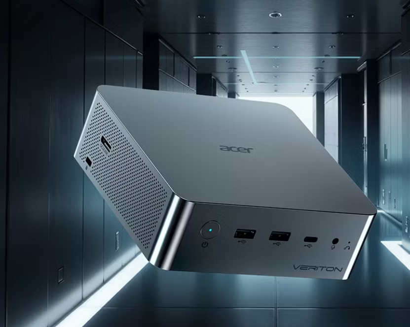 Рекламное изображение компактного ПК Acer Veriton RI110 серого цвета, расположенного под углом в пространстве. На передней панели видны круглая кнопка включения с индикатором, порты USB, разъем USB Type-C и аудиовыход 3.5 мм. На левой боковой грани виден порт OCuLink и вентиляционная перфорация. Компьютер изображен на размытом фоне коридора современного дата-центра с серверными стойками и неоновой подсветкой.